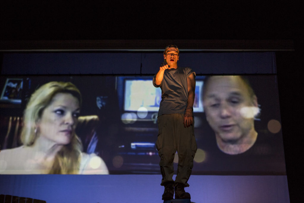 Actor Riley Suter, who plays the character Cole, stands center stage as a Skype interview with the real parents of Suter's character plays behind him. 