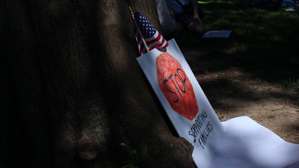 A sign reading stop separating families along with an American flag rests on a tree trunk in Lafayette square.