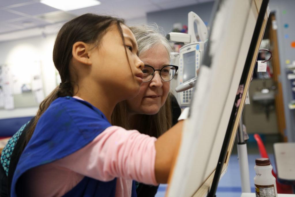 Tracy Councill, an alumna and art therapist, looks on as her patient Elise works on a painting of a dog. Elise has been working with Tracy since she was 2 years old.