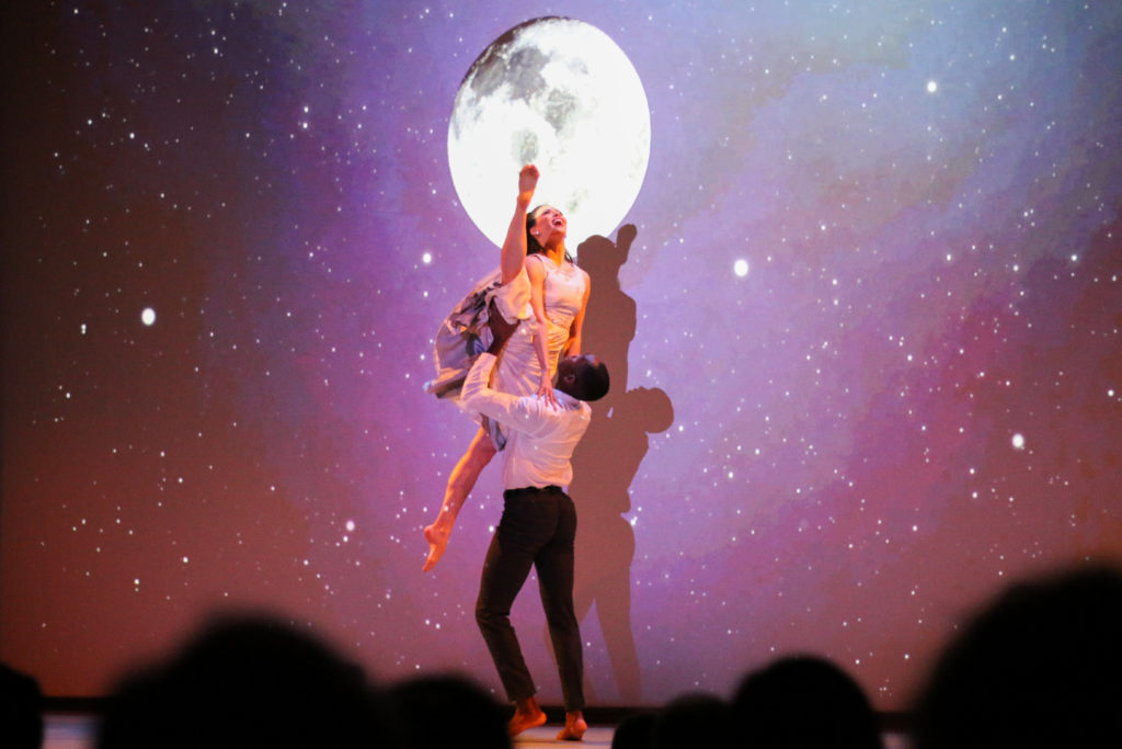Two dancers perform in front of an image of the moon provided by NASA during 