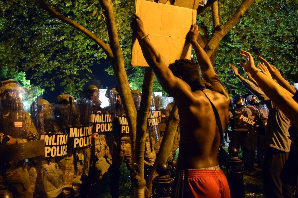 A protester holds up a sign in front of military police at Lafayette Square Park, located in front of the White House.