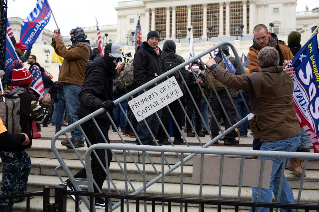 Rioters lift a fence picket in front of the U.S. Capitol Wednesday. The GW Program on Extremism is tracking those charged with criminal activity during the riot in a database launched Friday.