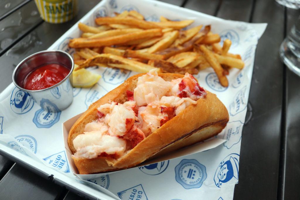 The lobster roll comes on a buttered, toasted bun with a lemon slice and a choice of greens or fries on the side.