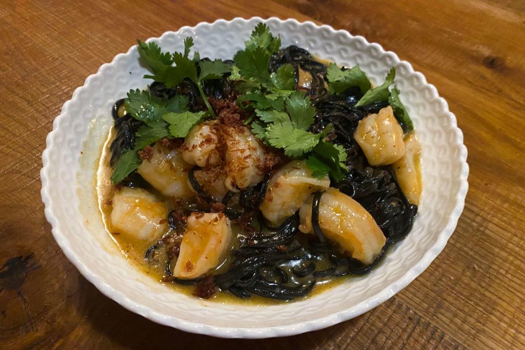 Served in a shallow ceramic bowl, the stark black capellini – similar to angel hair pasta – contrasts with the creamy yellow tint of the butter sauce and bright green leaves of cilantro.
