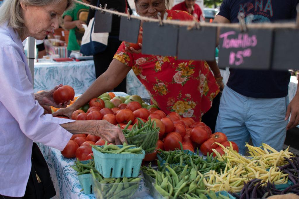 A woman reaches for produce at a booth at the Dupont Farmers Market Sunday. The farmers market sells food items from more than 50 farmers from across the region.