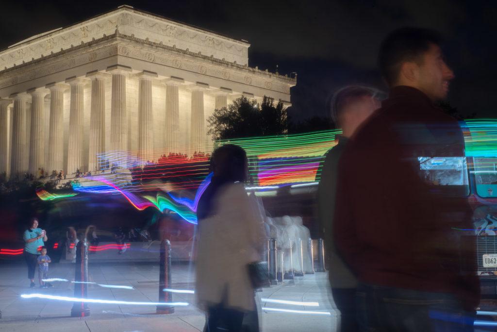 In an unusually warm start to November, a group gathers around an ice cream truck by the Lincoln Memorial Saturday as a streak of hoverboard riders speed by, leaving a rainbow of light marking their path. 