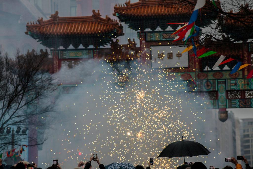Firecrackers explode in the air in bursts of light, leaving behind a cloud of smoke.