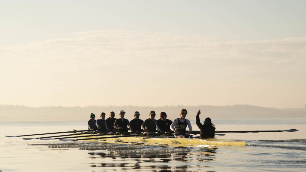 An eight-person boat full of the GW Mens Rowing team members sits atop the Potomac River as an early morning practice gets underway.
