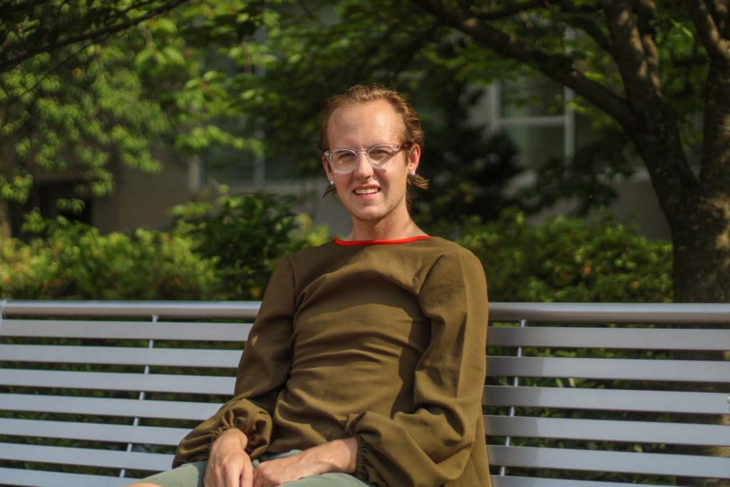 Graduating senior Cameron Cayer, sitting on a bench in Kogan Plaza, advises incoming freshman not to feel intimidated by spending time alone and embracing personal interests.