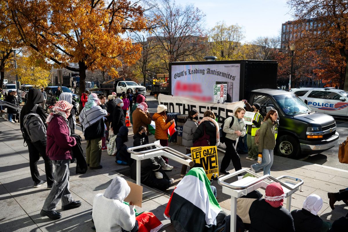 Pro-Palestinian protesters attempt to shield the names and faces of students flashing onto a billboard truck parked outside of the Elliott School. The Hatchet has blurred the name of the student projected onto the truck in post-production to preserve the individual’s privacy.