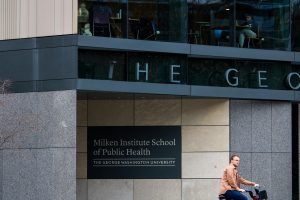 Commuters pass by the Milken Institute School of Public Health as students study inside.  