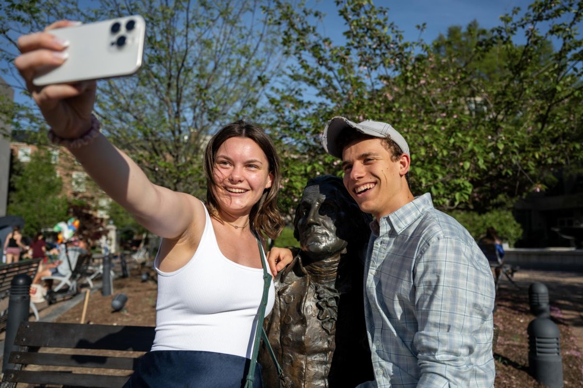 Two students pose for a selfie with the George Washington statue in Kogan Plaza. 