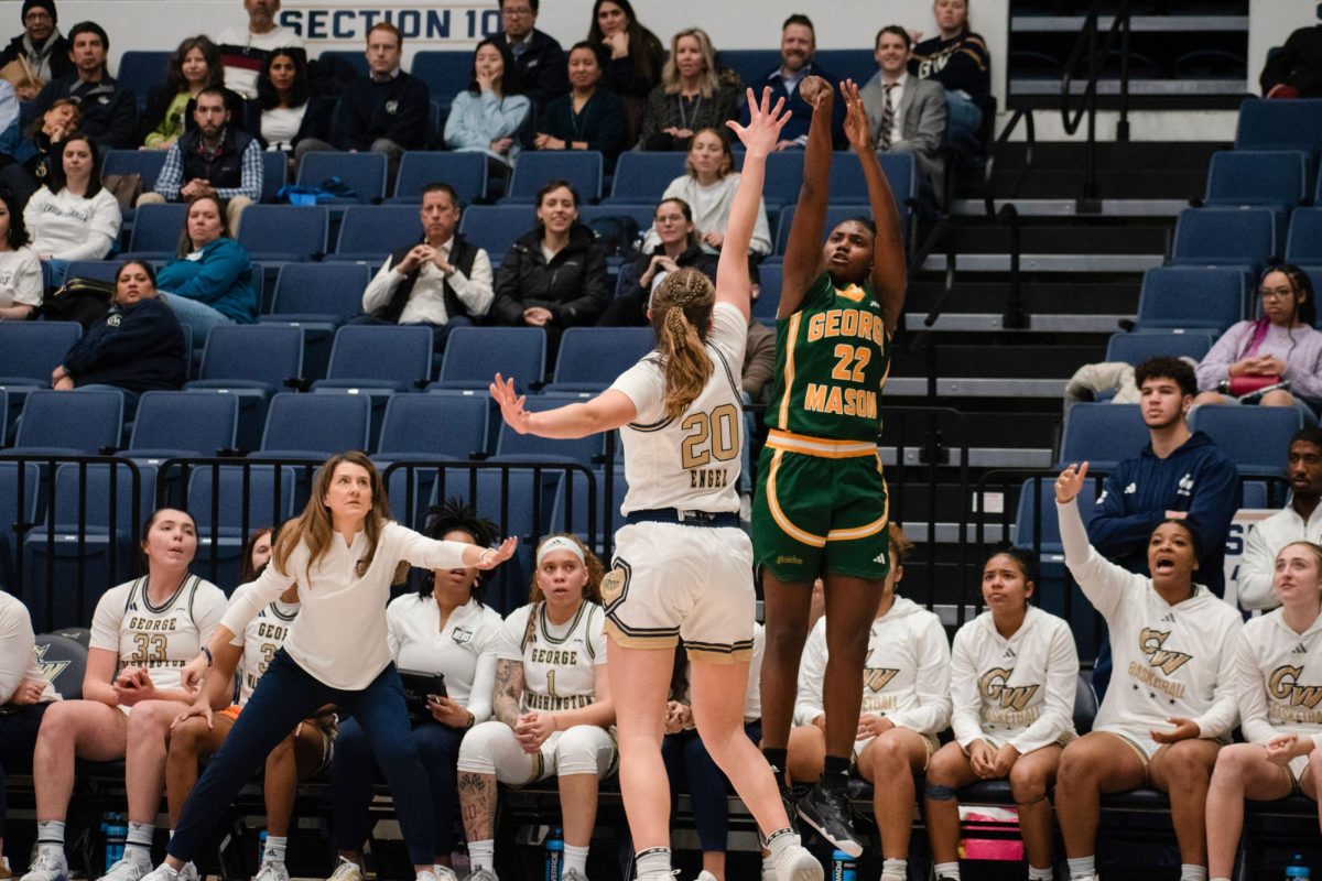 George Mason Guard TaViyanna Habib shoots over GW Forward Maxine Engel while the team watches from the bench.
