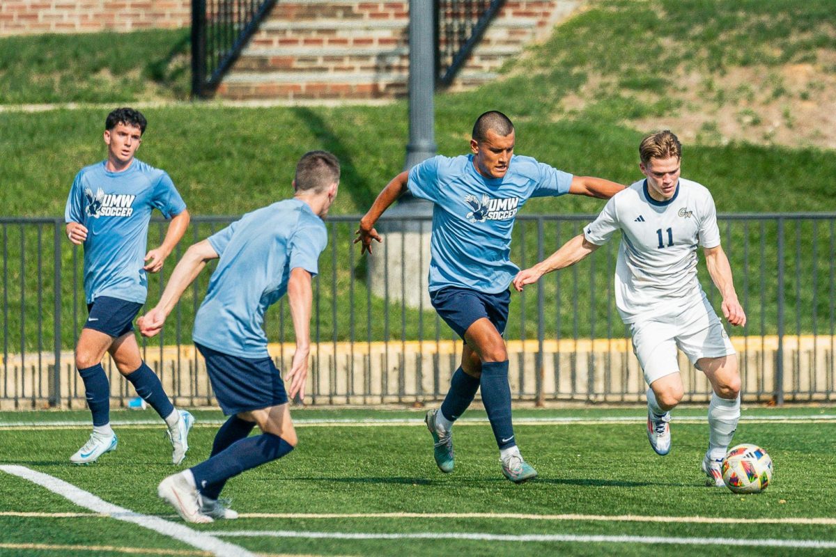 Sophomore midfielder Louis Saville kicks the ball while double teamed by two Mary Washington University defenders in August.