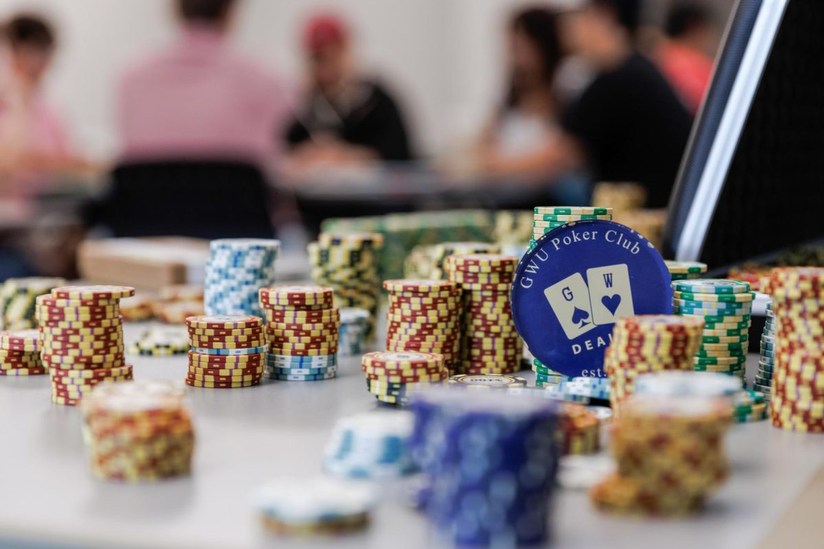 A poker chip with the GWU Poker Club's logo stands on a table surrounded by chips.