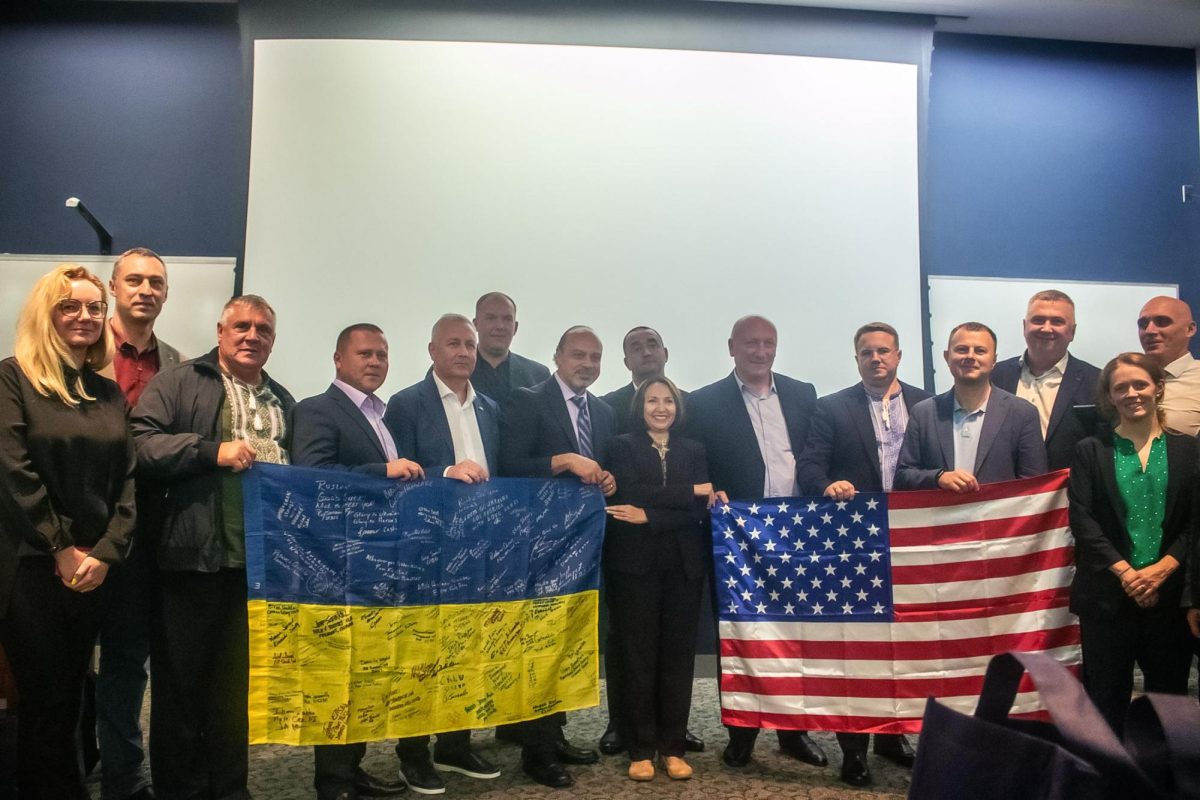 The Ukrainian mayors and event organizers pose for a photo holding the US and Ukraine flags.