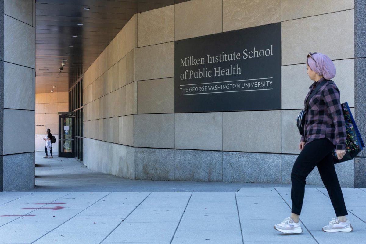 A student exits the Milken Institute School of Public Health as a person walks past.