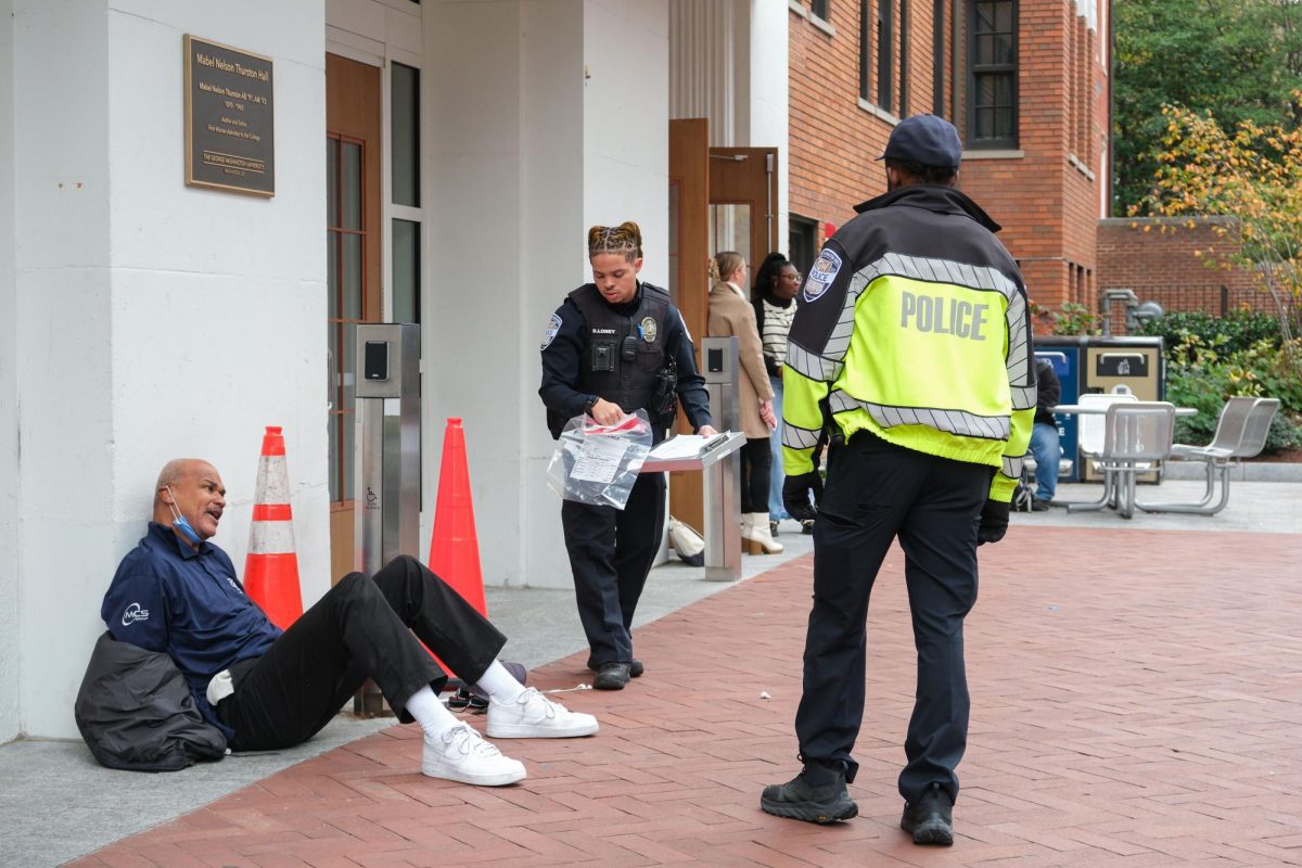 A GWPD officer collects evidence as the arrested employee sits cuffed against the Thurston Hall entrance.