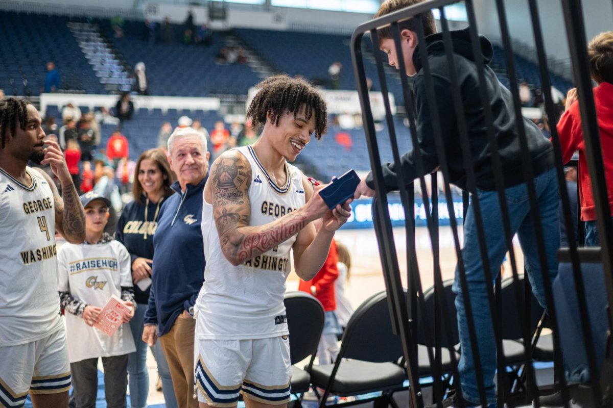 Redshirt junior guard Trey Moss autographs a young fan's book after the GW Men's Basketball Team's win against the Virginia Military Institute on November 29, 2024.