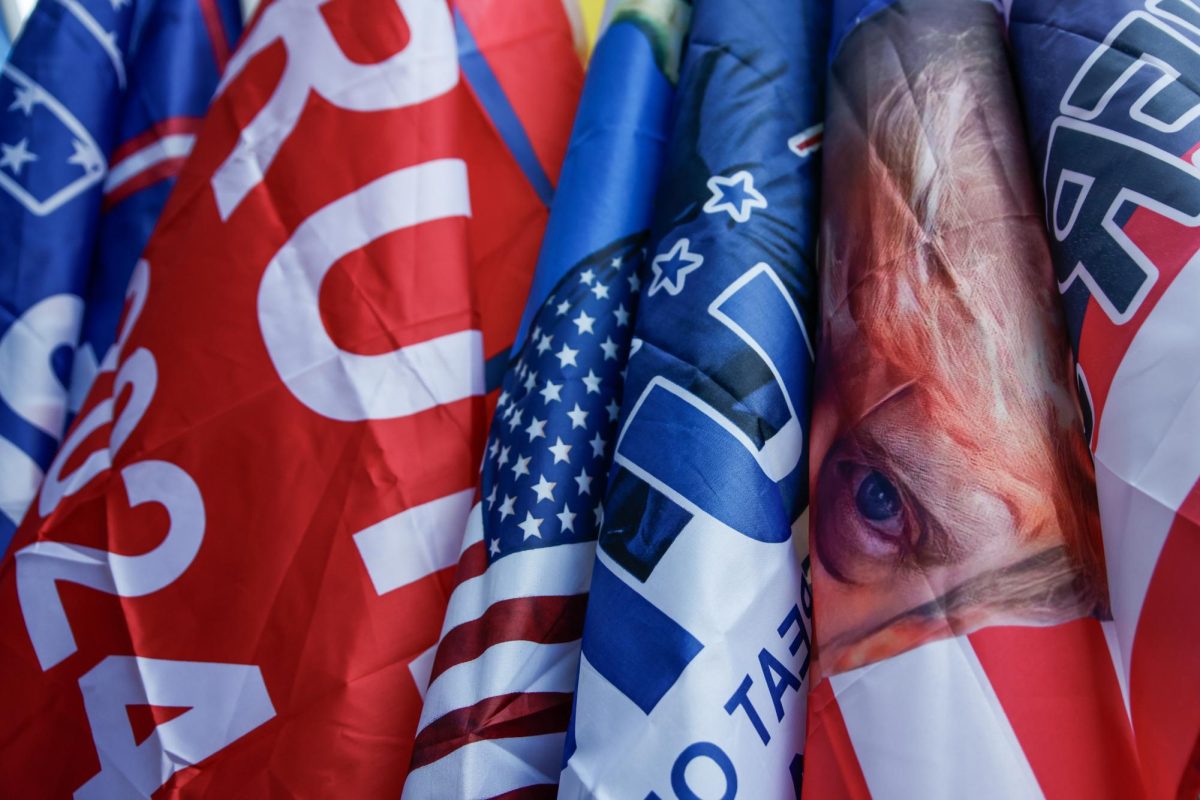 Flags bearing President Trump's face, name, and slogan wave against each other from a vendor stand in front of Capital One Arena on Inauguration Day.