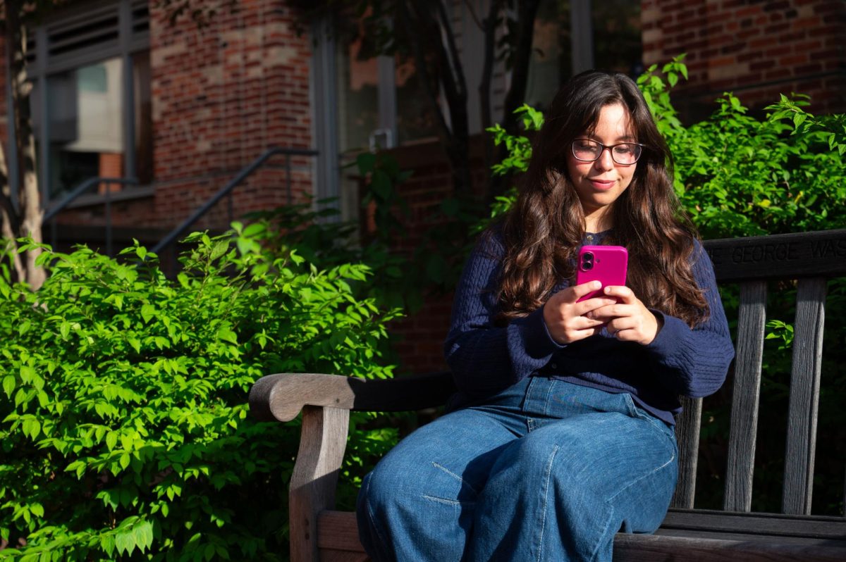 Marwa Medjahed sits on a bench in University Yard while scrolling on TikTok.