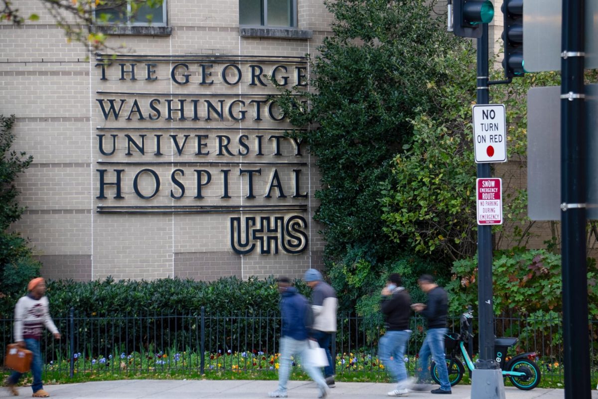 Pedestrians pass under the Universal Health Services sign on GW Hospital.